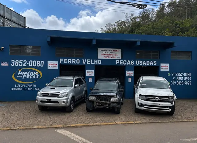 Fachada da Império das Peças vista da rua, com a parede azul, o logo e três caminhonetes na frente